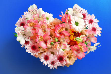 Composition of beautiful flowers in a heart shape on blue backgroundの写真素材