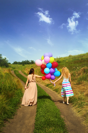 Happy women with colorful balloons on countryside roadの写真素材