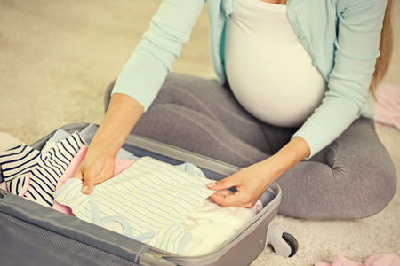 Pregnant woman packing suitcase for maternity hospital at homeの写真素材