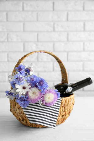 Wine bottle with flowers in basket on light backgroundの写真素材