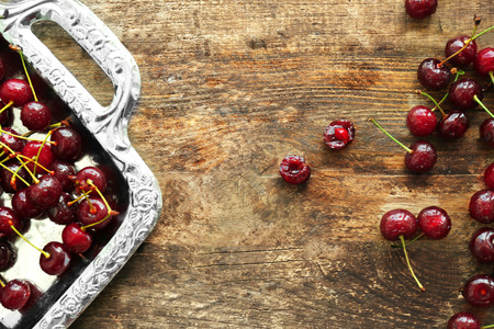 Old metal tray with ripe cherries on wooden backgroundの写真素材