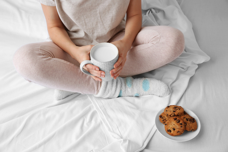 Woman having breakfast with cookies and cup of milk on the bed, close upの写真素材