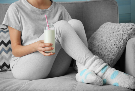 Woman with glass of milk on sofa, close upの写真素材