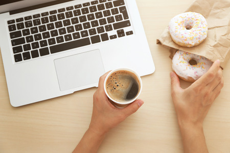 Female hands with laptop and cup of coffee on wooden backgroundの写真素材