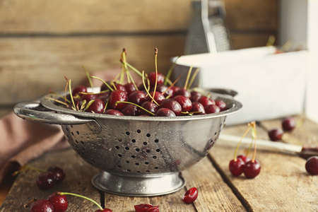 Cherries in colander on wooden tableの写真素材
