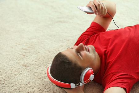 Young man listening to music on smartphone in the roomの写真素材