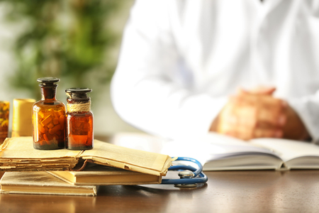 Medicines in bottles with old books and doctor on backgroundの写真素材