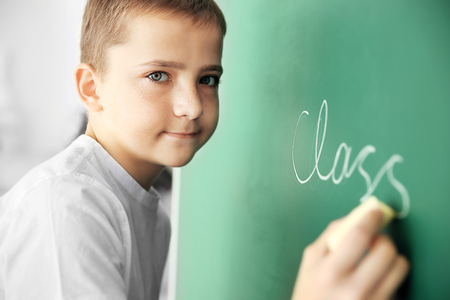 Cute schoolboy writing on chalkboardの写真素材