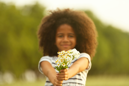 Happy little African American girl with flowers in the fieldの写真素材