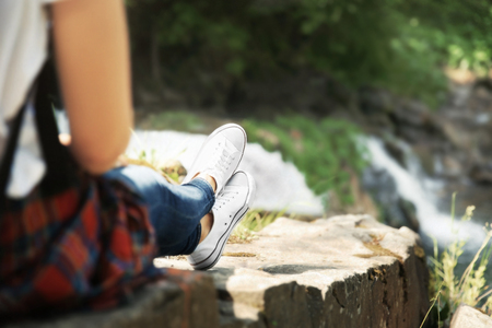 Female tourist sitting on stone beside the streamの写真素材