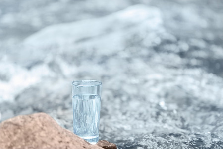 Glass of water on blurred river background