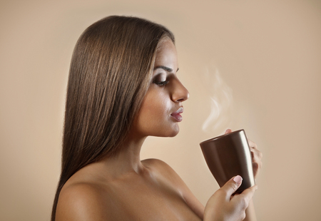 Beautiful young woman drinking coffee on color backgroundの写真素材