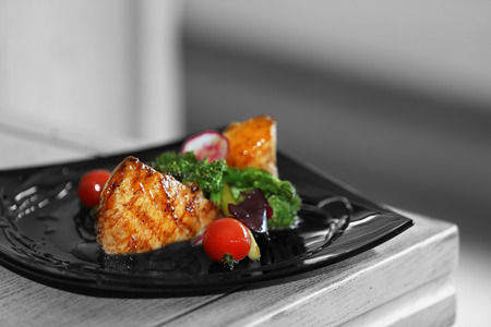 Fried chicken fillet with vegetables on black plate