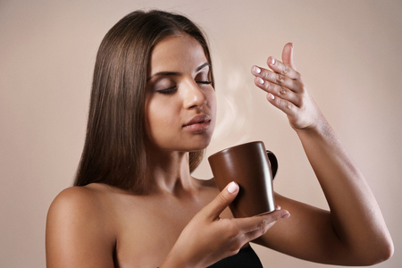 Beautiful young woman drinking coffee on color backgroundの写真素材