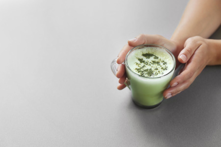 Female hands holding cup of green matcha tea on color background
