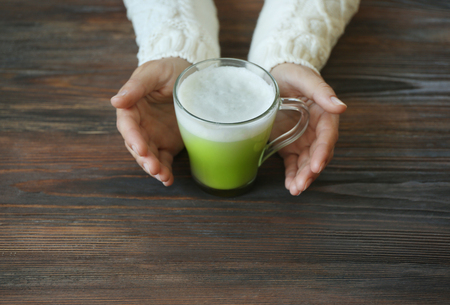 Female hands holding cup of green matcha tea on wooden backgroundの写真素材