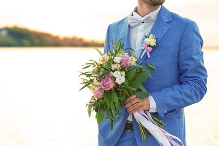 Groom with beautiful bouquet on sunset background