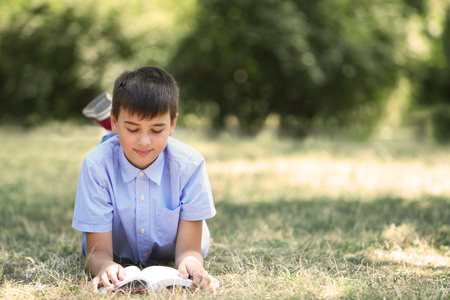 Cute boy reading book on green grassの写真素材