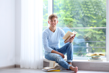 Young handsome man reading book at homeの写真素材