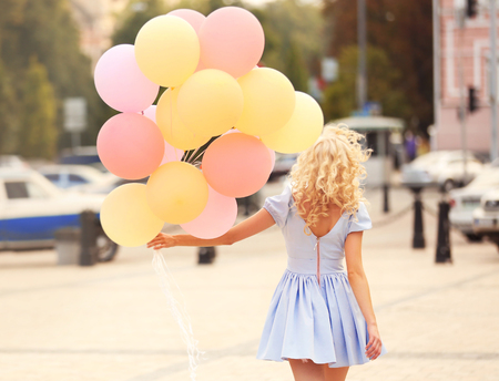 Beautiful young woman holding air balloons on streetの写真素材