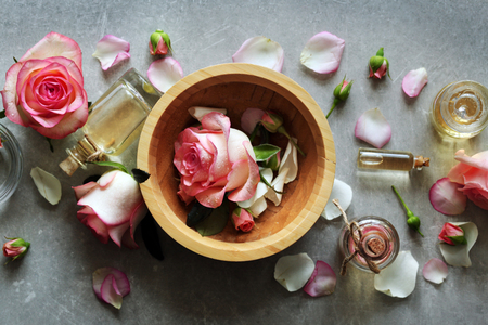 Bottle of aroma oil with roses in wooden bowl on tableの写真素材