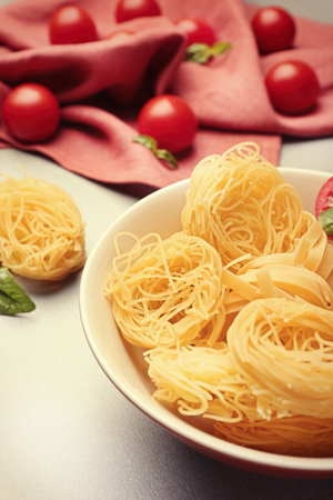 Bowl with pasta nests and cherry tomatoes on table, close upの写真素材