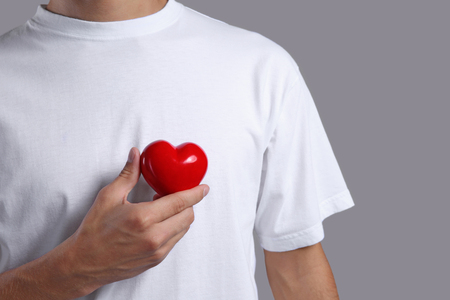 Young man with red heart on grey backgroundの写真素材