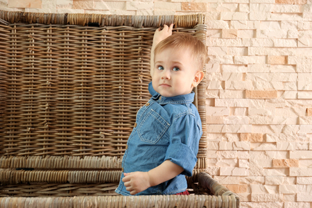 Stylish baby boy in denim shirt in a wicker basket on a stone wall background. Fashion conceptの写真素材