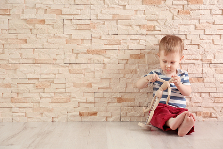 Stylish baby boy in a striped T-shirt with toy sitting on a stone wall backgroundの写真素材
