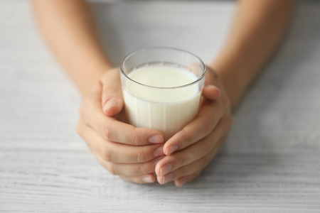 Female hands holding glass of fresh milk on light wooden backgroundの写真素材