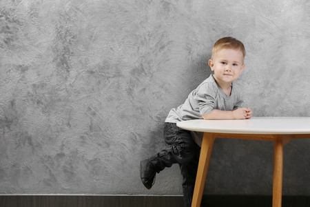 Stylish baby boy posing beside the table on the gray wall backgroundの写真素材