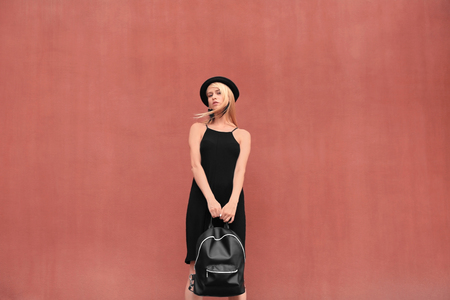 Stylish young woman in black dress with leather rucksack on brown backgroundの写真素材
