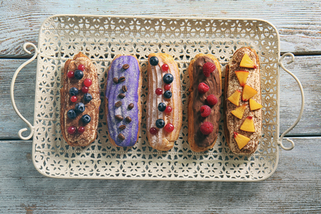Delicious colourful eclairs with berries and fruit on tray