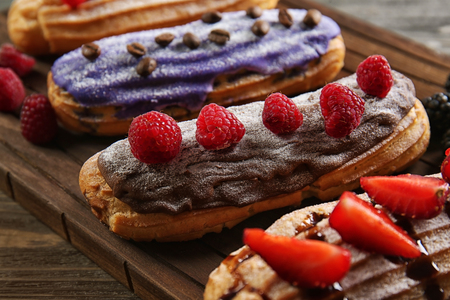 Delicious colourful eclairs with berries on wooden cutting boardの写真素材