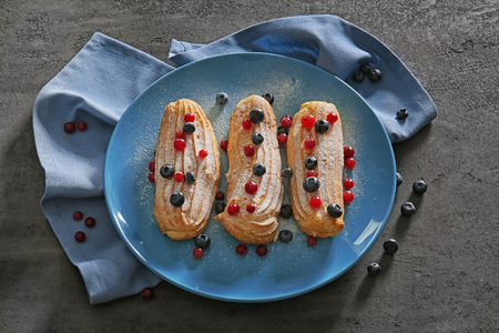 Tasty eclairs with berries on blue plate