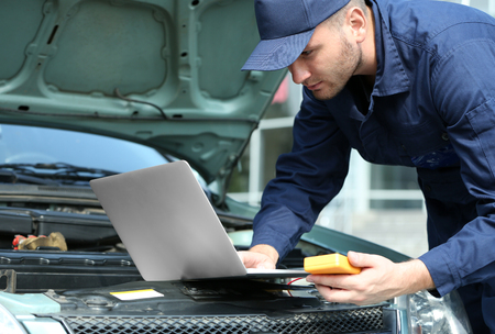 Mechanic using computer diagnostics while repairing carの写真素材