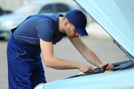 Mechanic standing in front of the open hood and repairing the carの写真素材