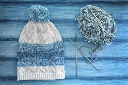 Knitted cap, ball of yarn and needles on wooden background