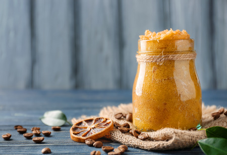 Glass jar with scrub, dried lemon slice and coffee grains on wooden tableの写真素材
