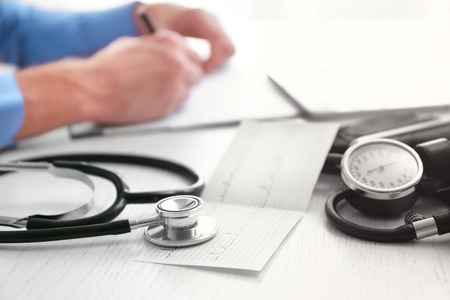Sphygmomanometer, cardiogram and stethoscope on doctor table, close up view