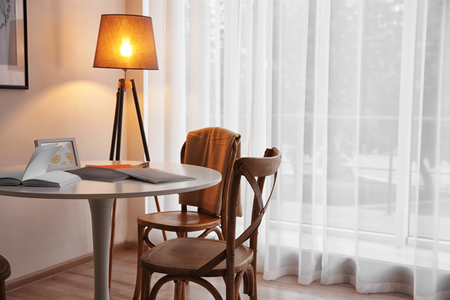 Modern white table, floor lamp and wooden chairs near windowの写真素材