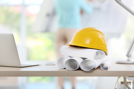 Helmet with blueprints and laptop on table and engineer on blurred backgroundの写真素材