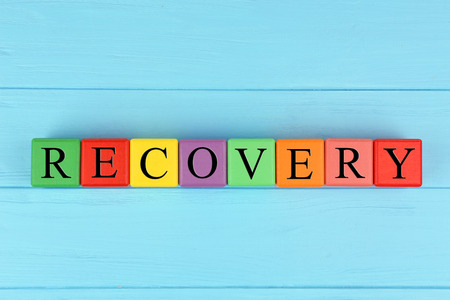 Word RECOVERY made of colourful cubes with letters on blue wooden backgroundの写真素材