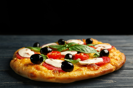 Delicious pizza with mushrooms, cherry tomatoes, olives and basil on blue wooden table and black backgroundの写真素材