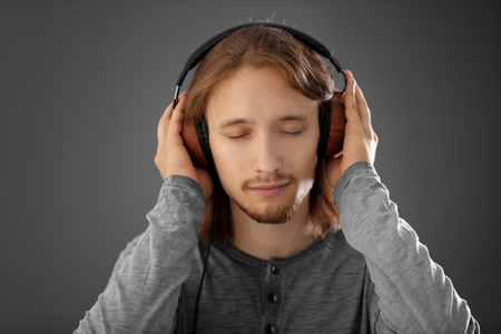 Handsome young man wearing headphones on grey backgroundの写真素材