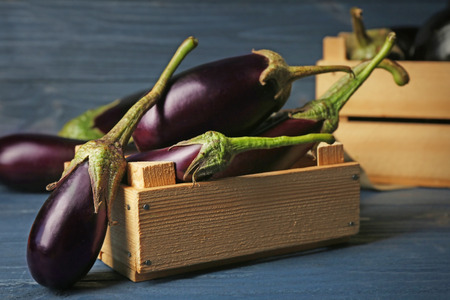 Fresh aubergines in crate on wooden backgroundの写真素材