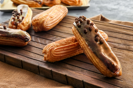 Delicious eclairs on wooden cutting board closeup