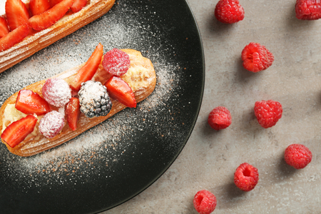 Delicious eclairs with berries and sugar powder on black plate
