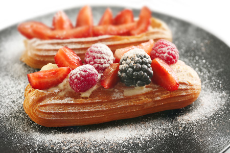 Delicious eclairs with berries and sugar powder on black plate