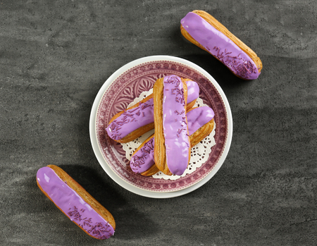 Plate with delicious glazed eclairs on dark textured background
